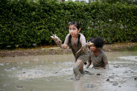 Two happy children child girl catching big frog in the large wet mud puddle on summer day.