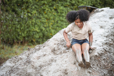 Happy African-American child girl playing on heap of wet soil during raining in rainy season.の写真素材