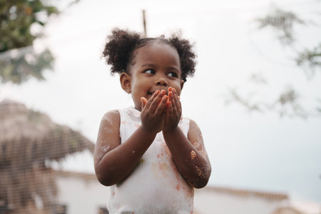African-American child holding chicken egg with color stain on hand and dress.