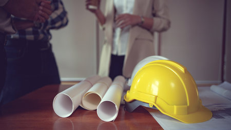 Close up view of engineer worktable with safety helmet and blueprint on desk in office room.の写真素材