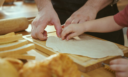 Happy young family enjoying making pie dough or pastries in modern kitchen together, very happy parents teaching little son how to cook bakery at home.の写真素材