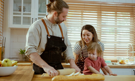 Happy young family enjoying making pie dough or pastries in modern kitchen together, very happy parents teaching little son how to cook bakery at home.の写真素材