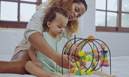Happy mother and daughter playing with a toy developing colorful wooden blocks on bed together at home.の写真素材