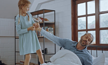 Daughter wakes up father at the bed in the morning.の写真素材