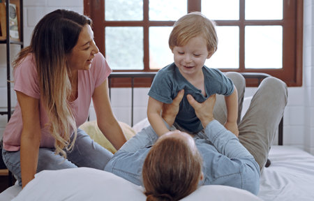 Happy family, mother, father and son laughing, playing on bed in bedroom at home.