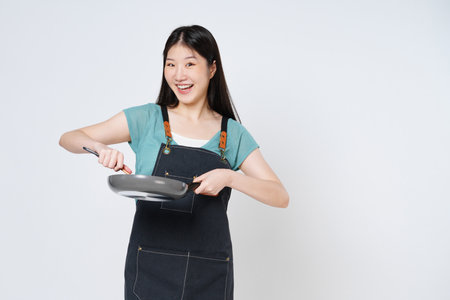 Young woman wearing kitchen apron cooking and holding pan and spatula isolated on white background.の写真素材
