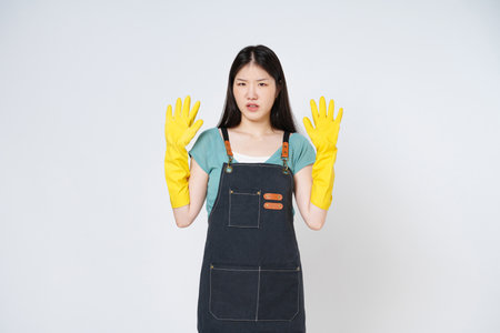 Portrait of young woman raised arms wearing apron and yellow rubber gloves standing isolated on white background.の写真素材