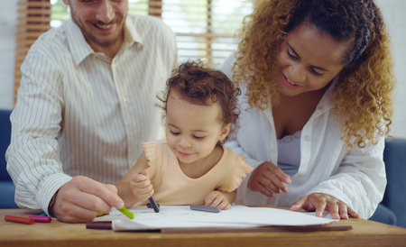 Dad, Mom and little daughter drawing with colorful pencils on paper happy smiling.Young family spend free time together in living room at home.の写真素材