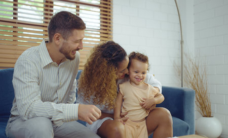 Happy cheerful parents having fun with cute daughter and hugging on sofa together, Enjoying family...