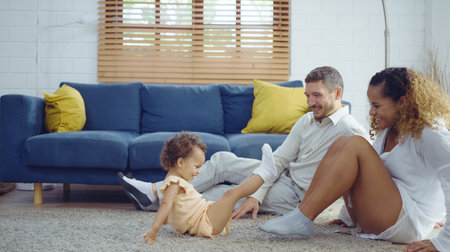 Parents warmth by embracing and teasing little daughter while spend time together on floor in living room at home. Mom and Dad using spare time with baby together at warmth house. Family concept.の写真素材
