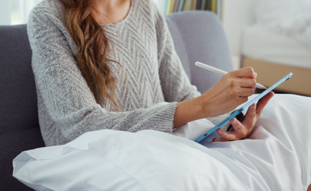 Asian young woman sitting on sofa using digital tablet and pen for learning shopping or working online at home.の写真素材