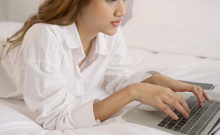 Young asian woman using and typing on laptop at bedroom.の写真素材