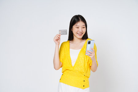 Happy young woman showing credit card while holding mobile phone isolated white background.の写真素材