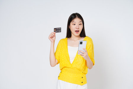 Happy young woman showing credit card while holding mobile phone isolated white background.の写真素材