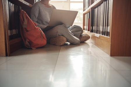 Student girl sitting on floor and using laptop, Writes notes for paper, Essay, Study for class assignment. Diverse group of Students Learning, Studying for Exams.の写真素材