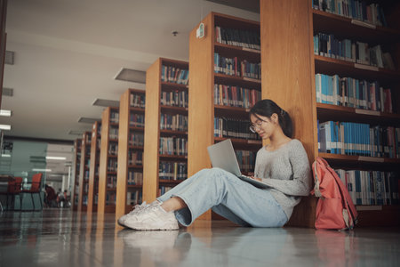 Student girl sitting on floor and using laptop, Writes notes for paper, Essay, Study for class assignment. Diverse group of Students Learning, Studying for Exams.の写真素材