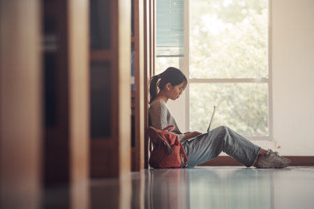 Student girl sitting on floor and using laptop, Writes notes for paper, Essay, Study for class assignment. Diverse group of Students Learning, Studying for Exams.の写真素材