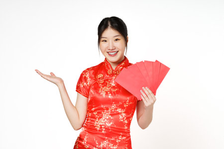 Asian woman wearing traditional cheongsam qipao dress showing something and holding angpao or red packet monetary gift isolated on white background. Happy Chinese new year.の写真素材