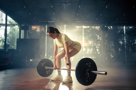 Young woman doing deadlift with heavy bar in gym, strong female athlete with muscular body lifting weights, exercising with barbell.の写真素材