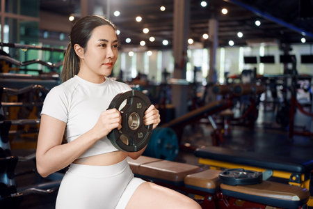Young asian woman doing exercises with heavy weights plates in gym.の写真素材