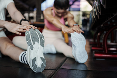 Fitness, stretching and two woman at gym for a warm up workout, training and body wellness with exercise. Young sports female or athlete on floor to stretch legs for strong muscle, balance and energy.の写真素材