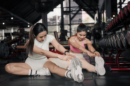Fitness, stretching and two woman at gym for a warm up workout, training and body wellness with exercise. Young sports female or athlete on floor to stretch legs for strong muscle, balance and energy.の写真素材