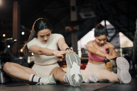 Fitness, stretching and two woman at gym for a warm up workout, training and body wellness with exercise. Young sports female or athlete on floor to stretch legs for strong muscle, balance and energy.の写真素材
