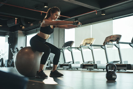 Sporty woman doing workout and using fitball by sitting and balancing on it.の写真素材
