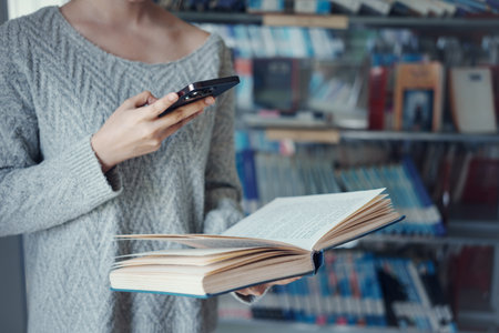Young asian female college student using a smartphone taking a photo of a book page in the school...