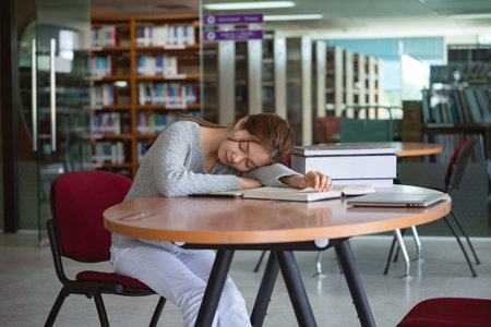 Tired woman student sleeping on desk in library.の写真素材