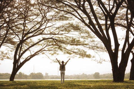 Young asian woman standing with arms raised on nature background.