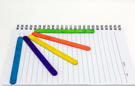 Colorful wood ice-cream stick  on Paper note book  on white backgroundの写真素材