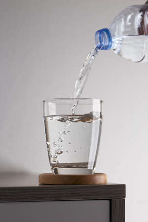 Water pouring from a plastic bottle in glass on wood table