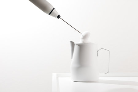 Making foamy milk with milk frother on a white table.の写真素材