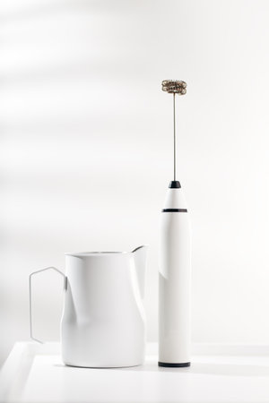 Milk frother and white pitcher for coffee on white minimalist table.の写真素材