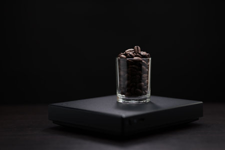 Dark roasted coffee beans in a clear glass on a black digital scale.の写真素材