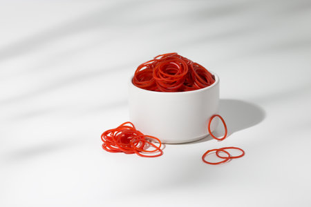 The large quantity of red rubber band is in a white ceramic bowl.の写真素材
