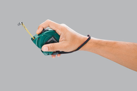 Male hand holding a tape measure on a gray background.