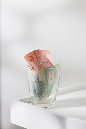 Tip money in a glass on a white dining table.の写真素材