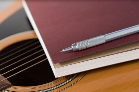 Pencil and notebook placed on acoustic guitar.の写真素材