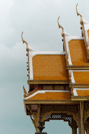 Ornate golden roofs of a Thai temple stand out on an overcast day, reflecting cultural heritage.