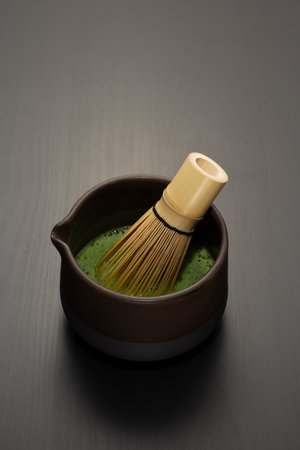A bamboo chasen whisk rests in a handcrafted chawan of vibrant green matcha, its frothy surface...