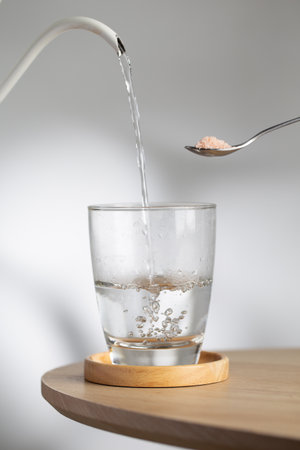 A spoon with himalayan salt beside a drinking glass as hot water pour inside, highlighting natural...