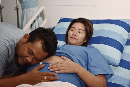Pregnant woman assisted by a doctor and nurse in a delivery room. Medical team examining pregnant woman during delivery while man holding her hand in operating roomの写真素材