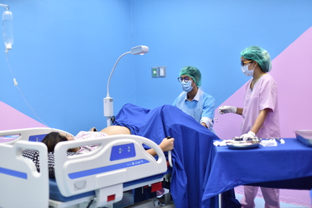 Pregnant woman assisted by a doctor and nurse in a delivery room. Medical team examining pregnant woman during delivery while man holding her hand in operating roomの写真素材