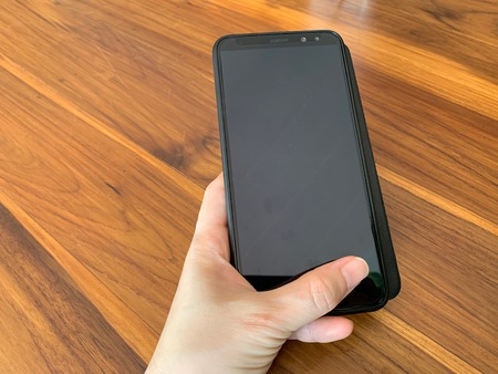 The hand of the person holding the mobile phone on the wooden table Wood background, mock up black...