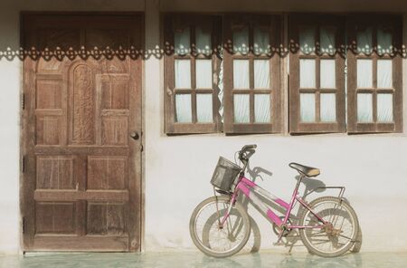 Old small bike leaning wall house with shadows of sunlight.の写真素材