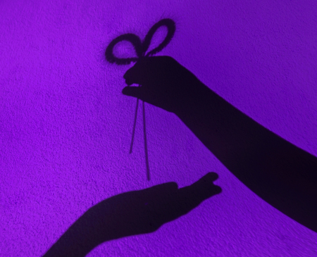 Blurry silhouette flowers in hand on violet background, Hand giving flower with love concept.の写真素材