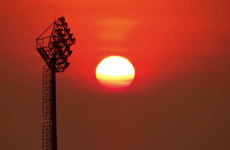Silhouetted of old stadium lights on blurred big sunrise background.の写真素材