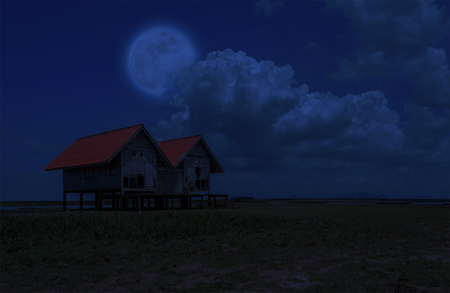 Twin old house on seashore at night which has full moon and cloudy on sky.の写真素材
